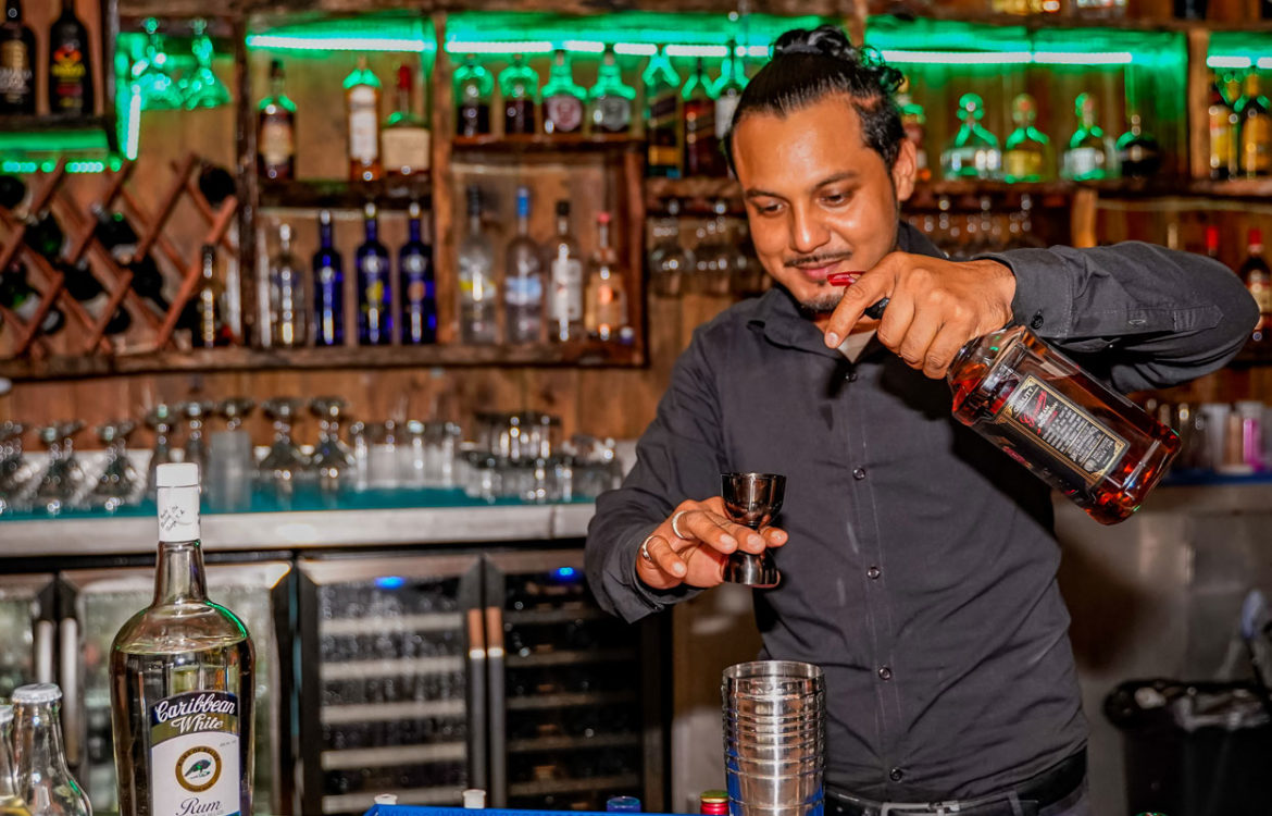 Bartender pouring a drink behind the best Caye Caulker bar at El Portal at the Split